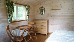 A wooden cabin room with a bed, a wooden desk, a chair, a dresser, and a window with curtains. - Långsjön Stugor & Camping (Ankarsrum)