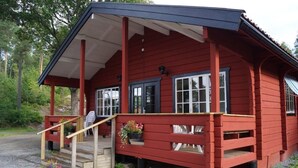 A red wooden building with a covered porch, steps, and potted plants. - Långsjön Stugor & Camping (Ankarsrum)
