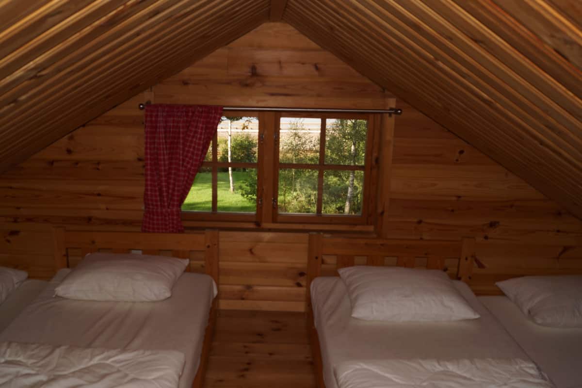 A cabin with two beds, a window with a red curtain, and a view of greenery outside.