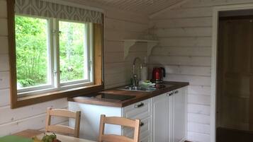 En stuga med träpanel på insidan, med ett köksområde, ett matbord och stolar.