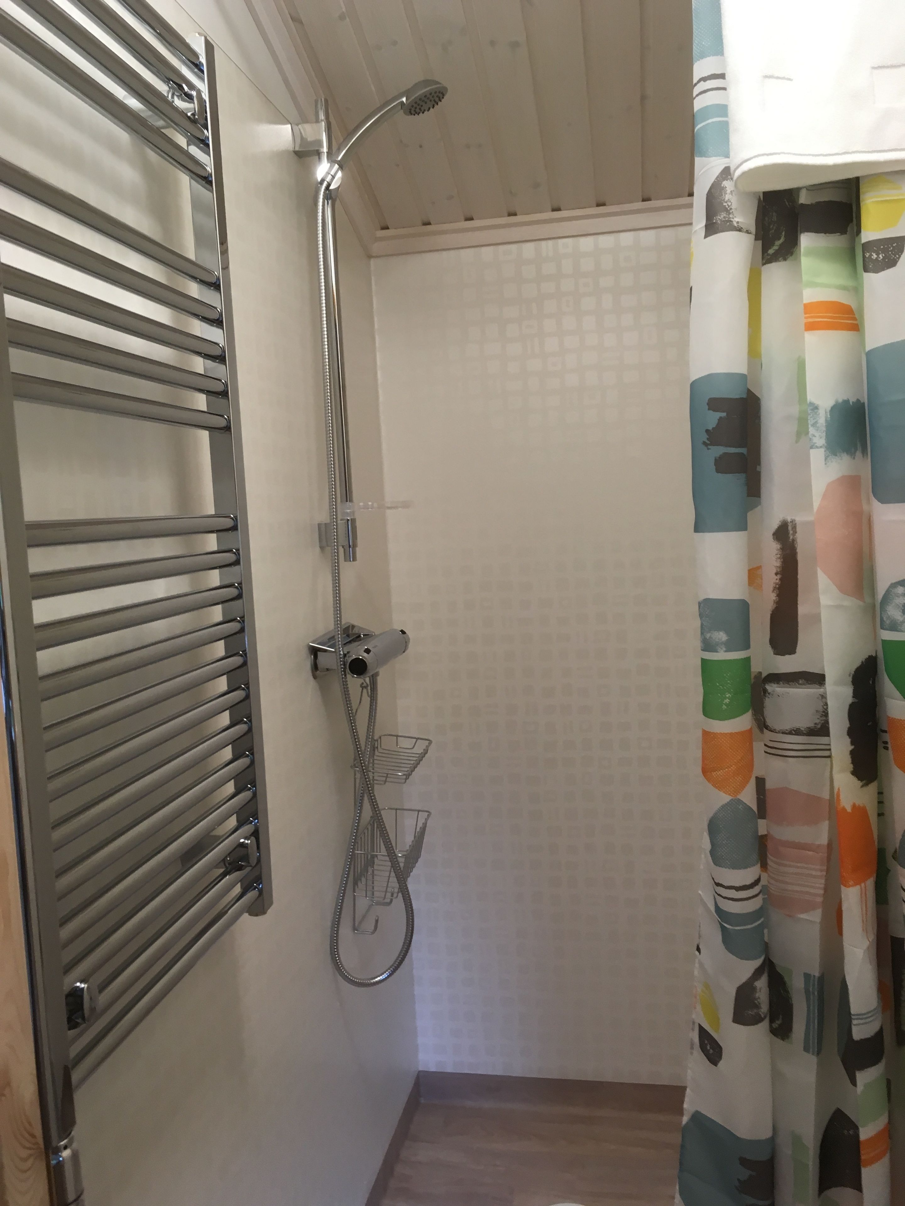 Et badeværelse med bruser, håndklædetørre og badeforhæng.