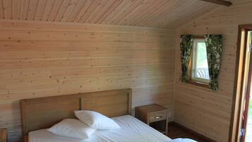 Habitación de cabaña de madera con una cama, una mesita de noche y una ventana con cortinas.