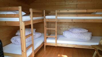 A wooden bunk bed room with three bunk beds, each with a pillow and a mattress.