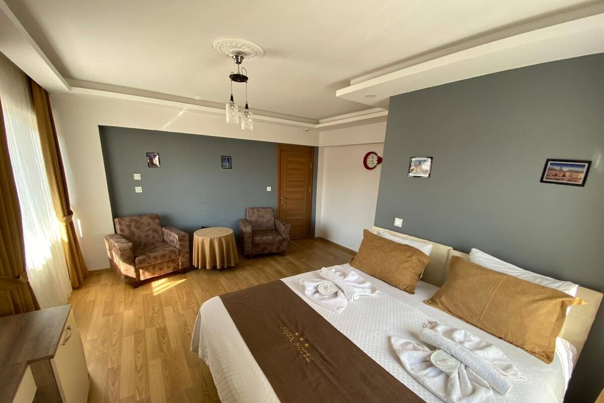 Une chambre d’hôtel avec un lit, deux fauteuils, une petite table ronde et un ventilateur de plafond.