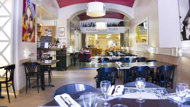 A restaurant interior with multiple dining tables and chairs, a wine rack on the wall, and a menu board. - Hotel Pinxo (Santa Coloma de Farners)