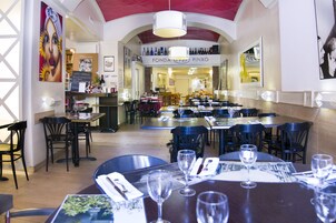 Un interior de restaurante con varias mesas y sillas, una estantería para vinos en la pared y una pizarra de menú.