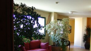 A living room with a red sofa, a large potted plant, and a wall-mounted TV. - Hotel Pinxo (Santa Coloma de Farners)