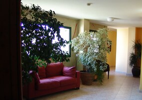 Una sala de estar con un sofá rojo, una planta grande en maceta y un televisor de pared.