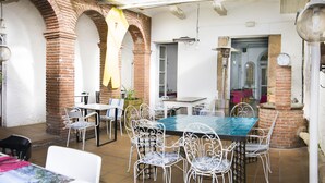 A dining area with a brick wall, white metal chairs, and a table with a blue tablecloth. - Hotel Pinxo (Santa Coloma de Farners)