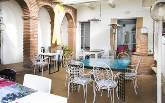Un comedor con pared de ladrillo, sillas metálicas blancas y una mesa con mantel azul.