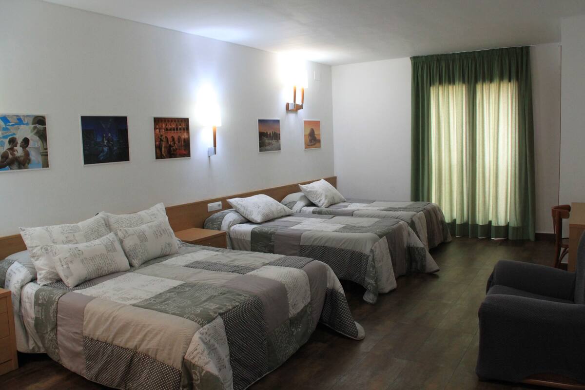 A hotel room with two beds, a chair, a nightstand, and wall art.