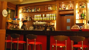 A bar with multiple liquor bottles and a coffee machine. There are red bar stools and a person behind the bar. - Hotel Pinxo (Santa Coloma de Farners)