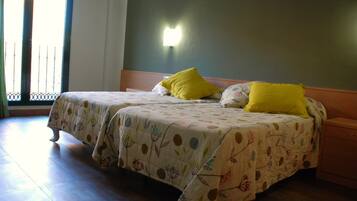 A double bed with floral bedding and two yellow pillows, a wooden nightstand, and a wall-mounted light fixture.
