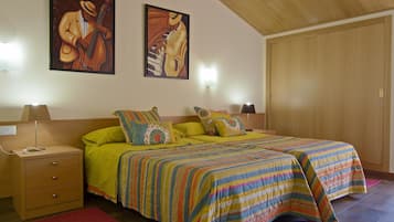 A bedroom with two beds, a wooden wardrobe, a nightstand with a lamp, and two wall-mounted lamps.