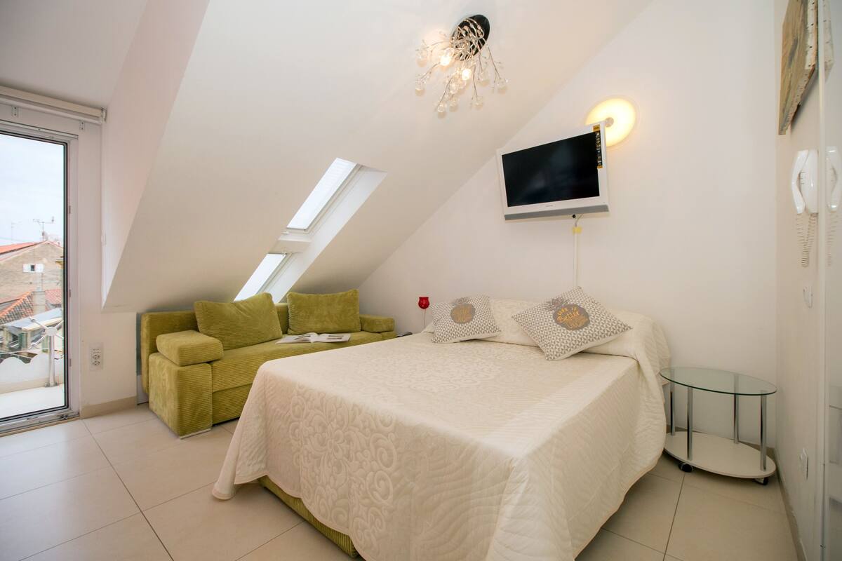 A bedroom with a bed, a green sofa, a TV, and a glass table.