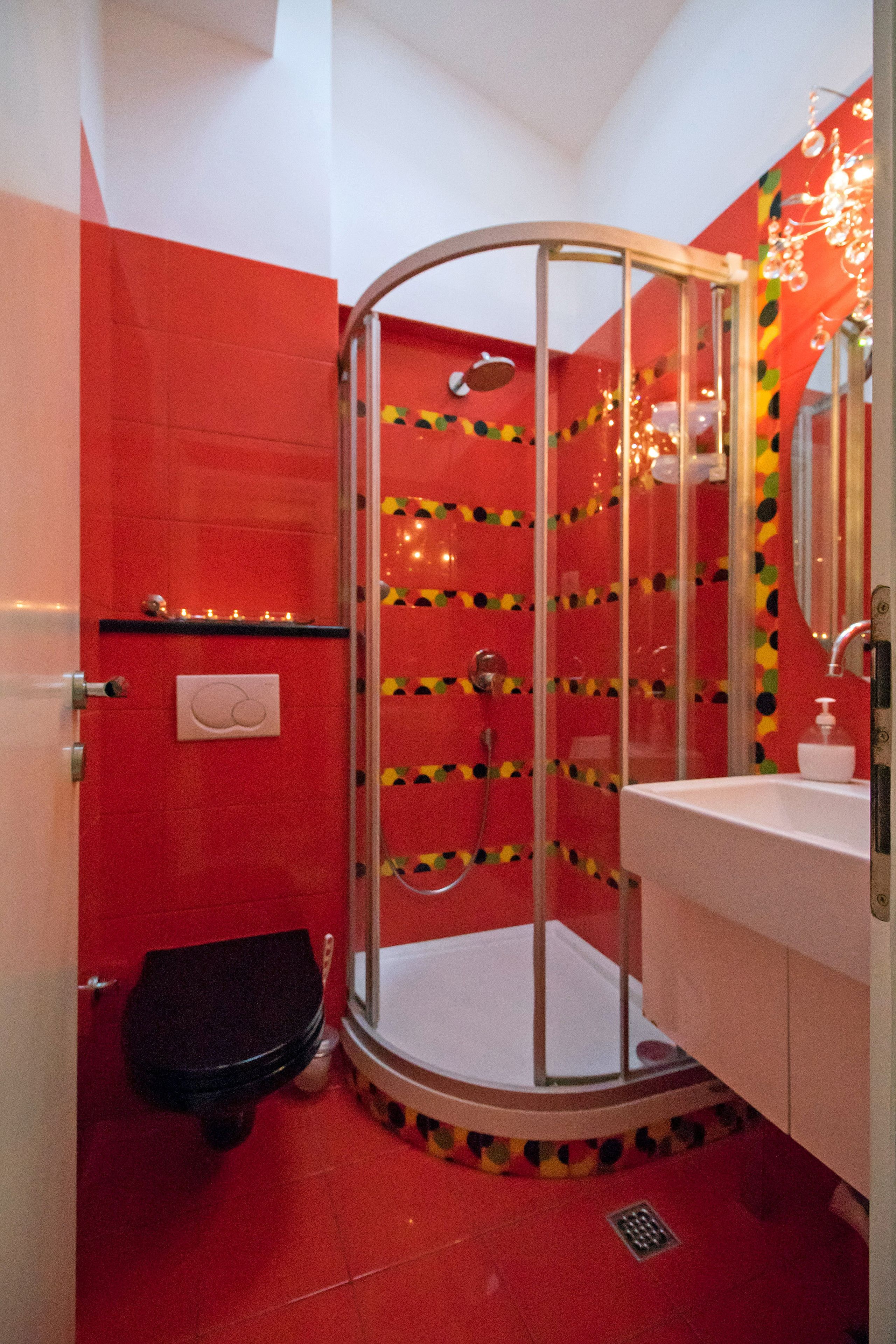 A bathroom with a glass shower enclosure, a white sink, and a red tiled wall.