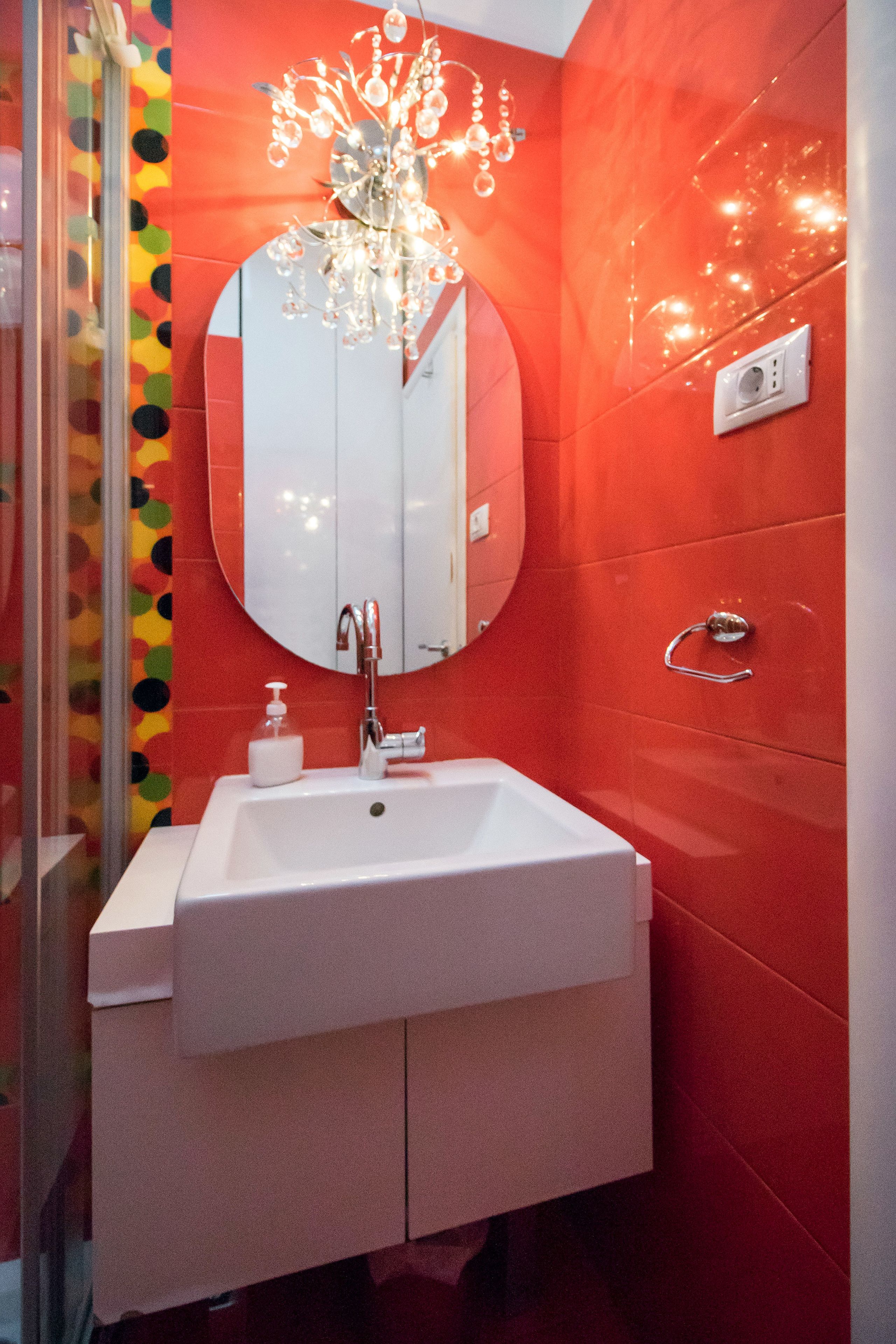 A bathroom with a white sink, a round mirror, and a chandelier.