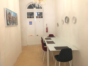 A conference room with a white table, black chairs, a red chair, a painting, a door with glass panels, and a fire extinguisher. - Gorgeous Townhouse Nr 53 - Hostel (Sliema)