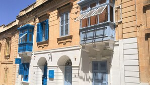 Una hilera de edificios con contraventanas azules y fachadas blancas, que presenta arcos en las entradas y una puerta central.