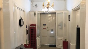 Un pasillo con un teléfono rojo, una araña y una puerta con un letrero.