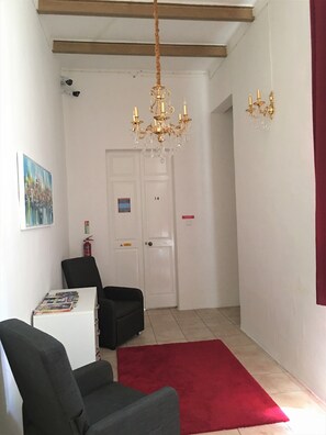 A hallway with a chandelier, a red rug, a black chair, a white cabinet with magazines, and a door marked with the number 14. - Gorgeous Townhouse Nr 53 - Hostel (Sliema)