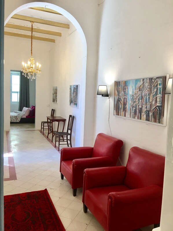 A spacious living area with a red sofa, a chandelier, and a painting of buildings on the wall. - Gorgeous Townhouse Nr 53 - Hostel (Sliema)