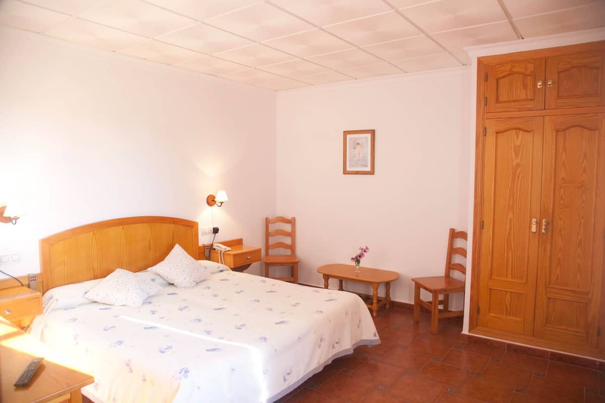 Une chambre à coucher comprenant un lit, une table de chevet, une lampe, deux chaises, une petite table et une armoire.