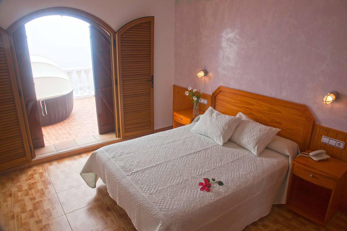 Une chambre à coucher comprenant un lit, une table de chevet, une lampe de chevet et donnant sur un balcon extérieur.