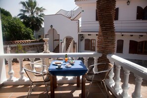 A terrace with a table set for two, chairs, and a view of a building with a balcony. - Hostal Mar de Frente (Barbate)