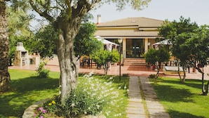 A house with a tiled roof, a paved pathway, and a garden with various plants and flowers. - B&B Villa Grazia (Alghero)