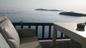 A balcony with a view of the sea, a white table, and a cushioned seating area. - Blue Waves View (Andros)