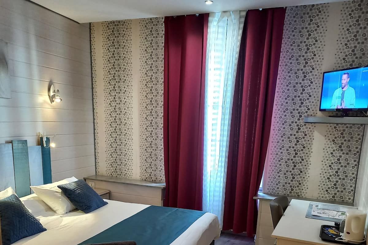 Une chambre d’hôtel avec un lit, un bureau, une télévision et une fenêtre avec des rideaux.