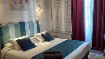 A modern bedroom with a large bed, a nightstand, a wall-mounted light, and a window with curtains.