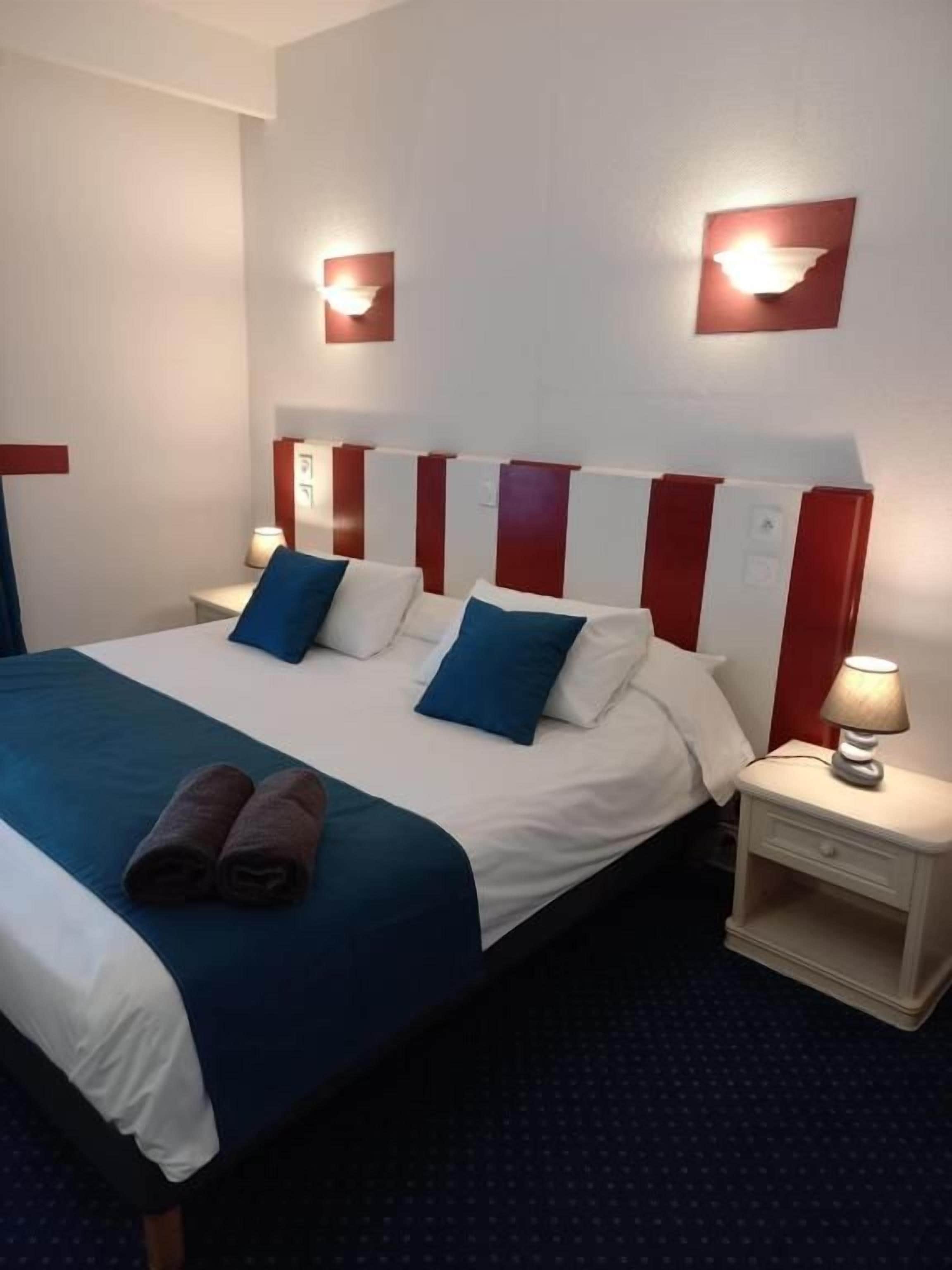 A hotel room with a bed, pillows, a nightstand, and a lamp.