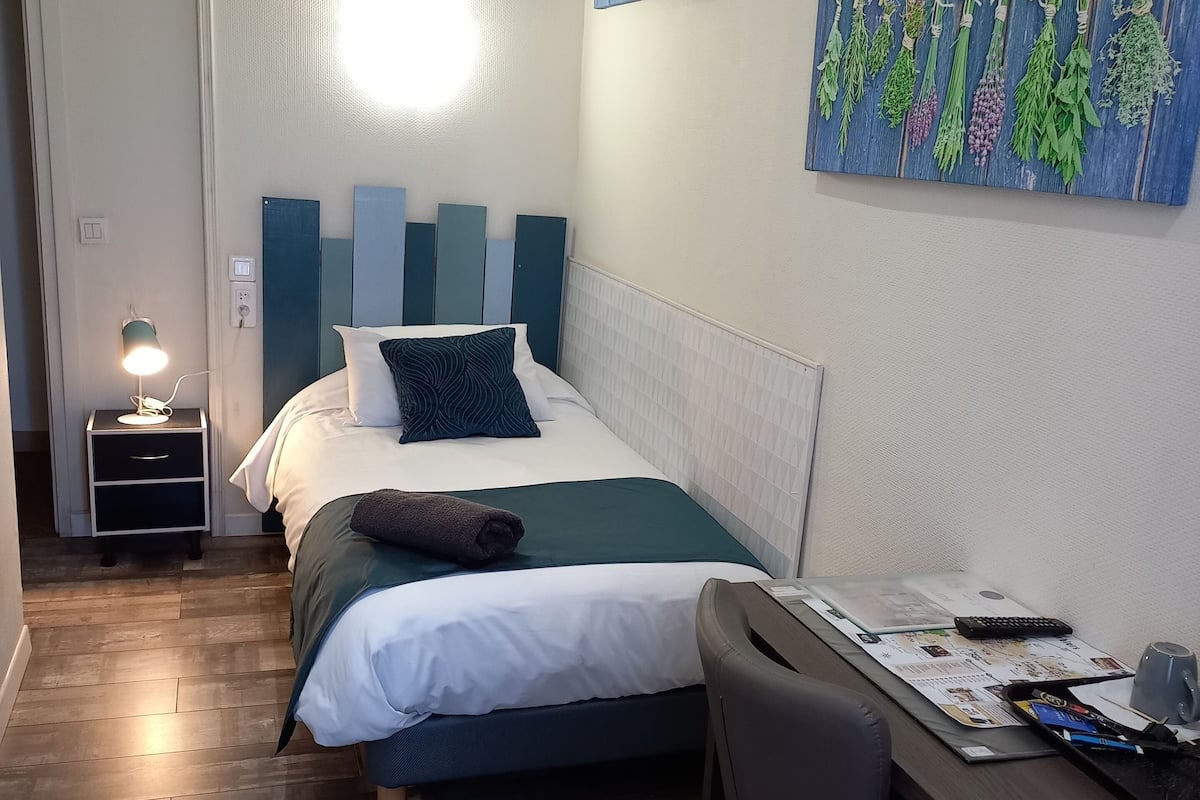 Une chambre d’hôtel comprenant un lit, un bureau, une chaise, une table de chevet avec une lampe et des œuvres d’art accrochées aux murs.