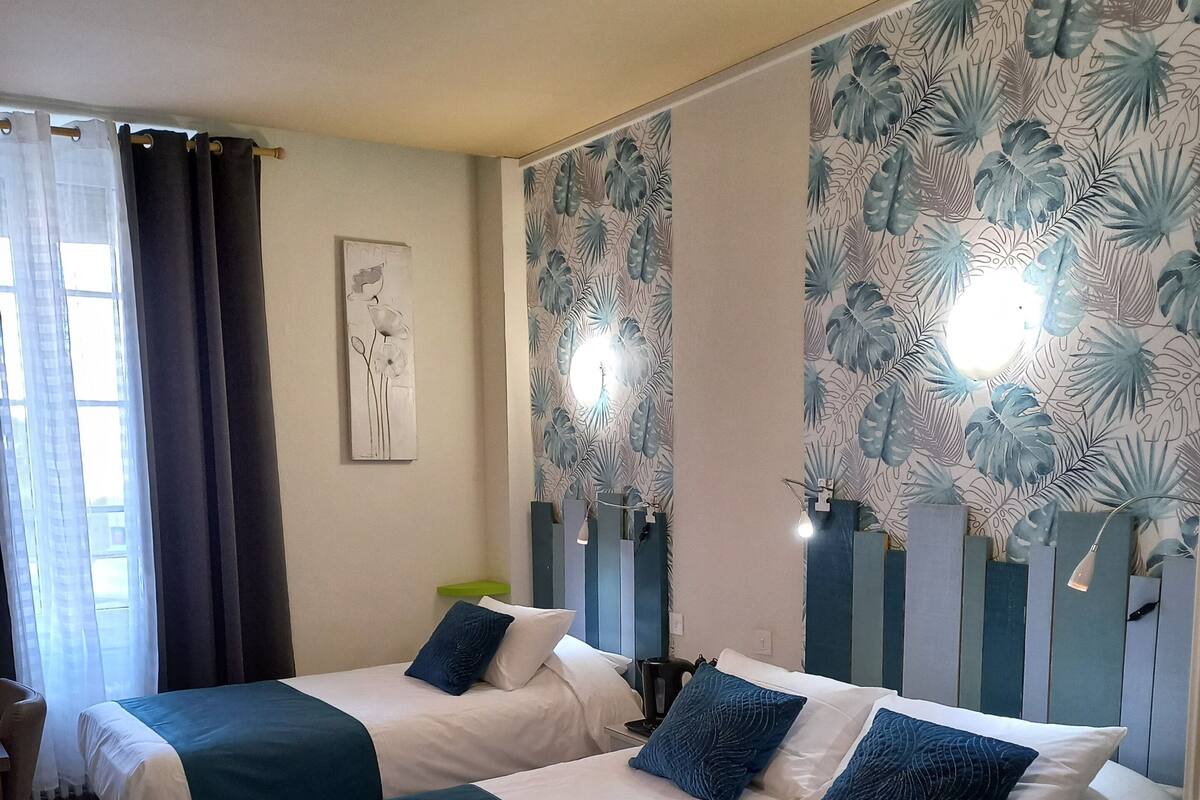 Une chambre d’hôtel avec deux lits, un plancher en bois, un mur recouvert d’un papier peint à motifs tropicaux et un tableau accroché au mur.