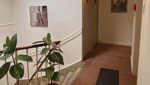Un pasillo de hotel con una escalera, plantas en macetas, un aplique decorativo y cuadros en las paredes.
