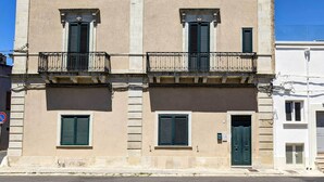 Ein zweistöckiges Gebäude mit symmetrischer Fassade, das einen zentralen Eingang mit einer grünen Tür und zwei Balkone mit schmiedeeisernen Geländern zeigt.