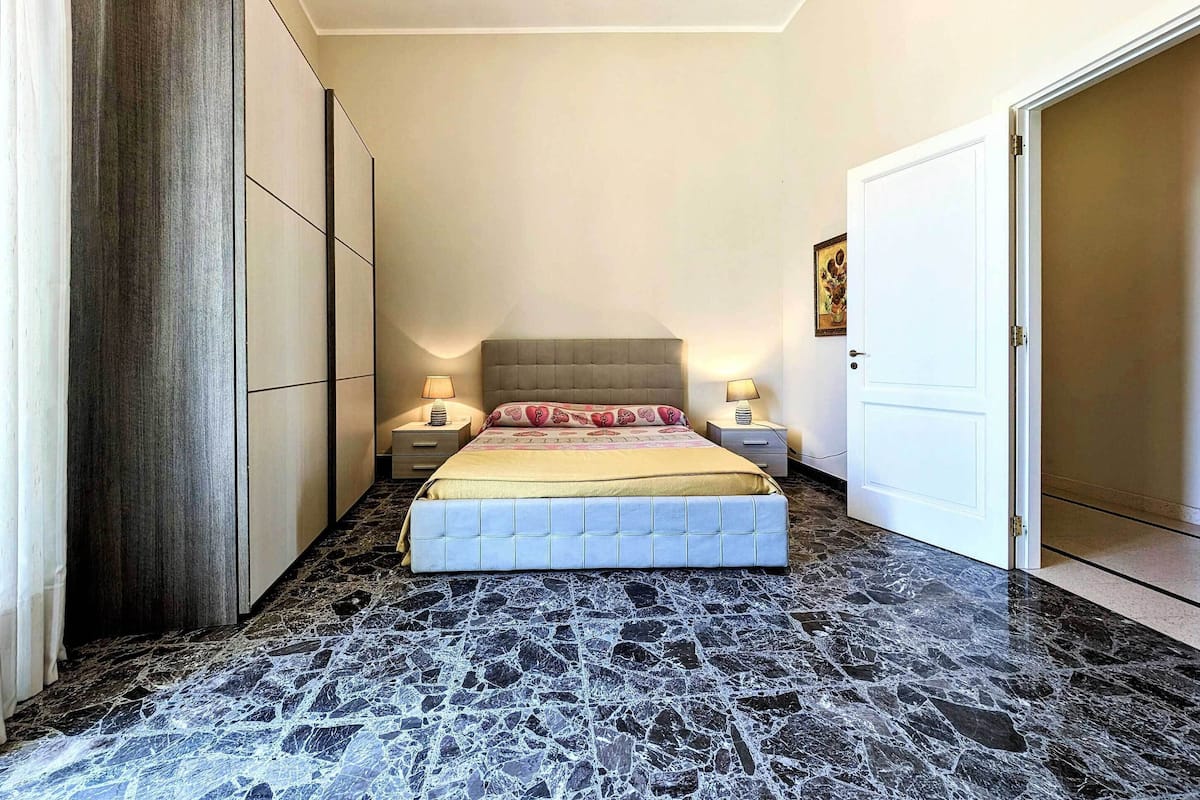 Un dormitorio con cama, dos mesitas de noche, un armario y una puerta.