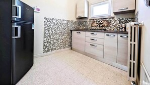 Eine kleine Küche mit einem schwarzen Kühlschrank, einer Mikrowelle und einer gefliesten Spritzschutzwand.