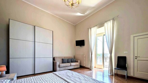 Ein Schlafzimmer mit einem großen Bett, einer Couch, einem Fernseher und einer Schiebetür zum Balkon.