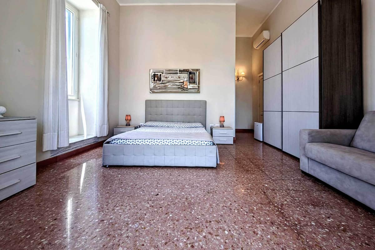 Un dormitorio con cama, dos mesitas de noche, un sofá, un armario y una obra de arte en la pared.