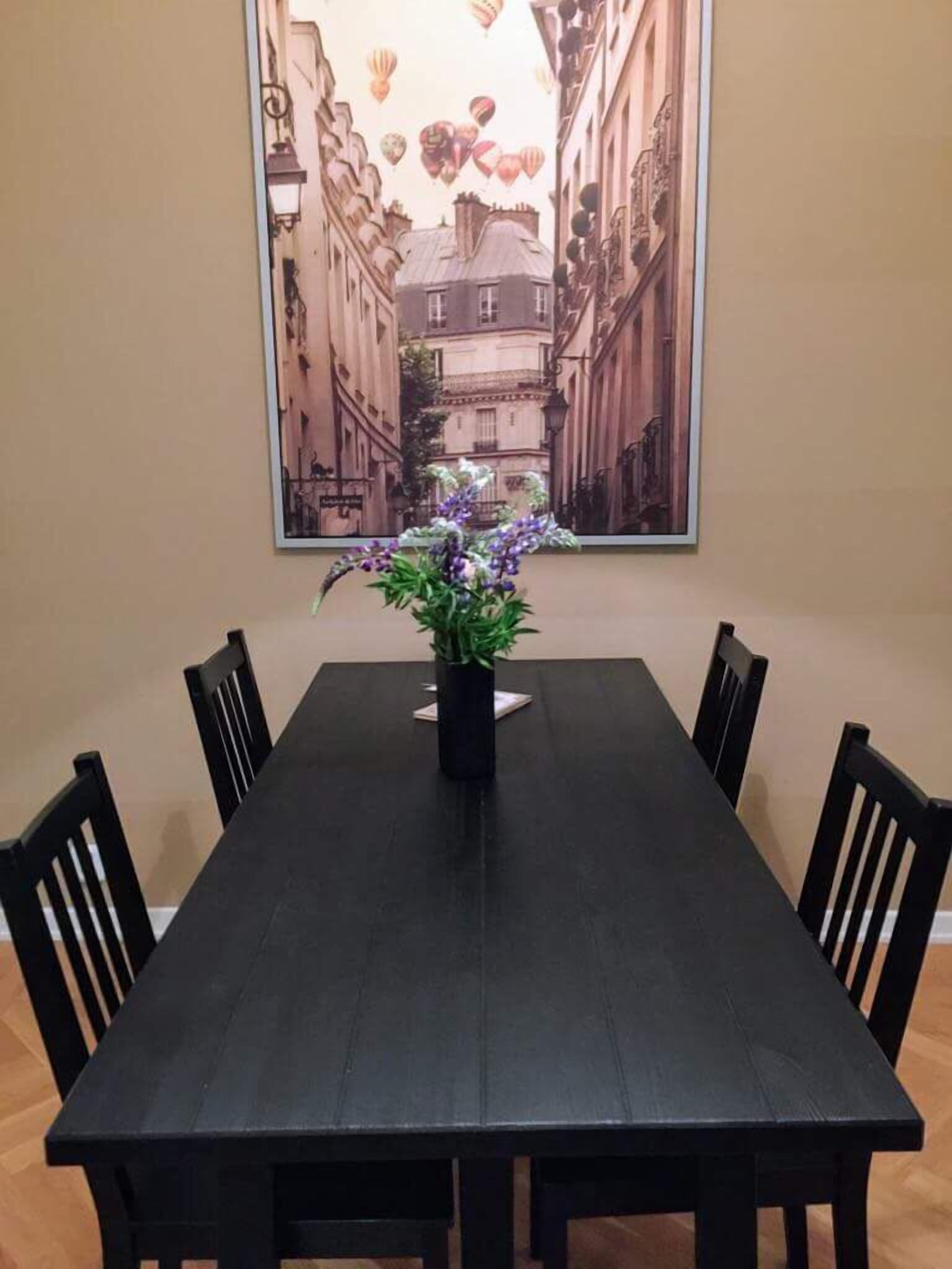A dining table with a vase of flowers in the center, surrounded by chairs.
