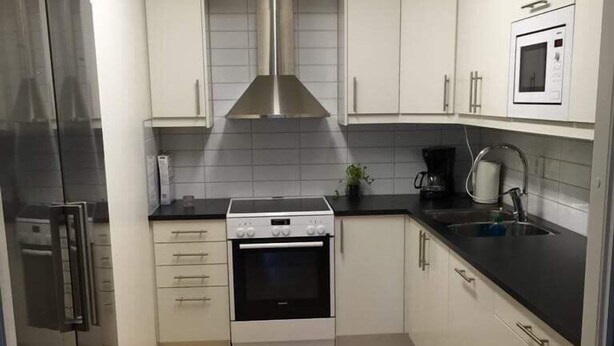 A compact kitchen with white cabinets, a stainless steel range hood, a built-in oven, a microwave, and a refrigerator. - Eklanda Heden (Gothenburg)