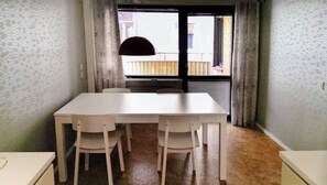 A dining area with a white table and chairs, a window with curtains, and a view of a balcony.