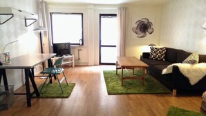 A modern living room with a sofa, a dining table, a TV, and a green rug. - Eklanda Apartment Lilla Bommen (Gothenburg)