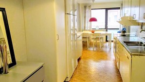 A compact kitchen with white cabinets, a refrigerator, and a dining area with a table and chairs. - Eklanda Apartment Lilla Bommen (Gothenburg)