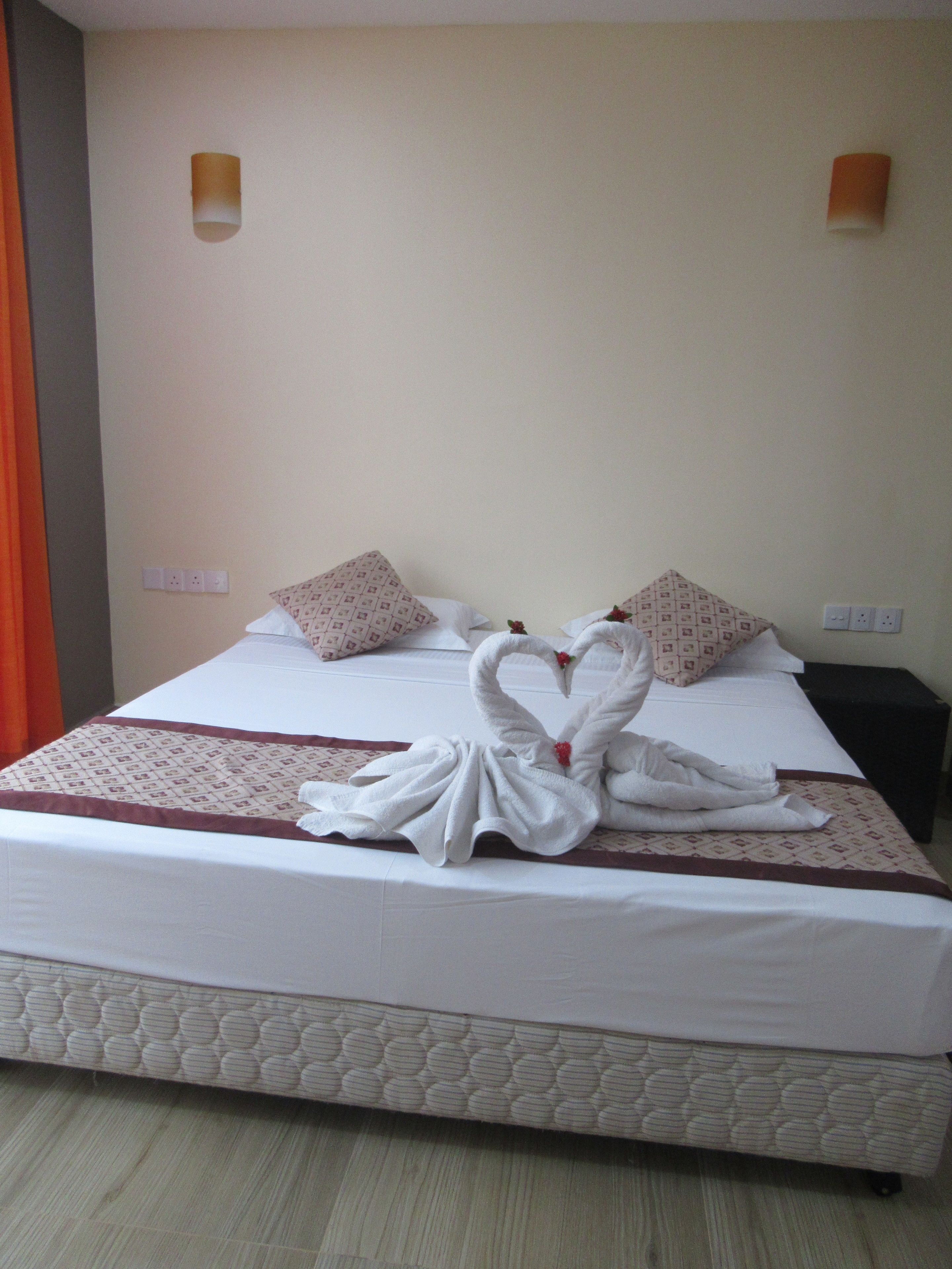 A hotel room with a neatly made bed, two pillows, a bedside table, and a wall-mounted lamp.