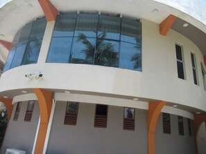A modern building with large windows reflecting palm trees, a curved facade, and multiple small windows with shutters. - Sand Bank Hotel & Restaurant (Tangalle)