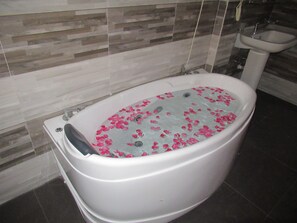 A bathtub filled with water and rose petals, a white sink, and a tiled wall. - Sand Bank Hotel & Restaurant (Tangalle)